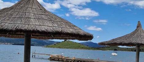 A beachside view with thatched umbrellas, a stone pathway, and calm water.