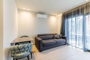 Ein modernes Wohnzimmer mit einer Couch, einem Esstisch mit einem außergewöhnlichen Stuhl und einem großen Fenster mit Vorhängen.
