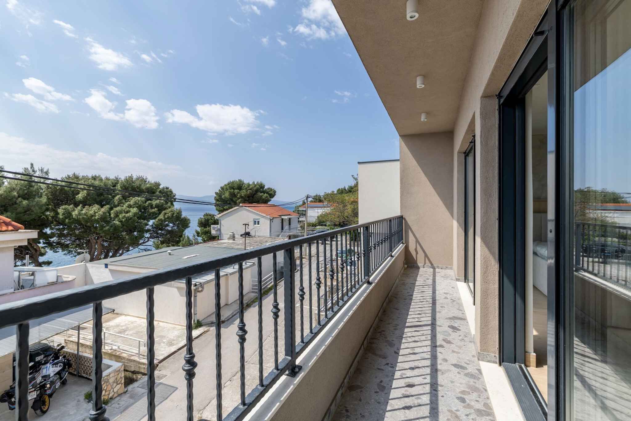 A balcony with a metal railing, a clear view of the sea, and a building with large windows.