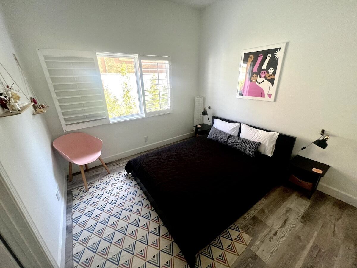 A bedroom with a bed, a chair, a window with blinds, a radiator, and a wall-mounted picture.