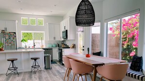 Een moderne keuken met witte kastjes, een eetgedeelte met roze stoelen, en een groot raam met roze bloemen.
