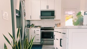 Een moderne keuken met witte kasten, een magnetron, een oven en een potplant.