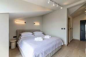 Ein modernes Schlafzimmer mit einem großen Bett, Nachttischlampen und einer sichtbaren Tür.