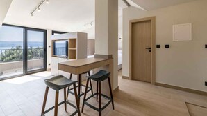 A modern kitchen with a large island, bar stools, and a view through the sliding glass door. - Holiday Apartment Studio Ela 3 (Stanići)