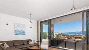 Ein modernes Wohnzimmer mit einer Couch, einem Gemälde und Blick ins Freie.