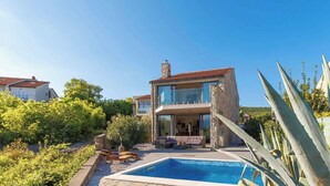 Ein modernes, zweistöckiges Haus mit Swimmingpool, umgeben von Grünflächen und einer Steinmauer.