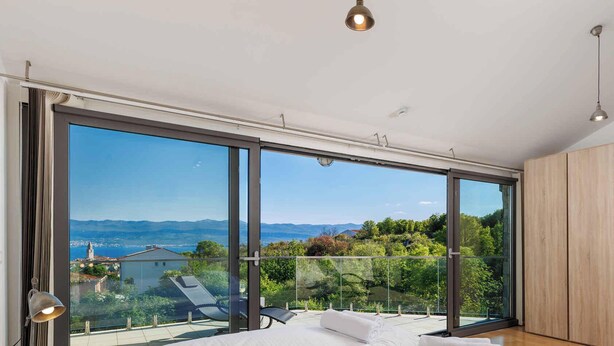 Ein modernes Zimmer mit großen Glasfenstern, die auf einen Balkon mit schöner Aussicht führen.