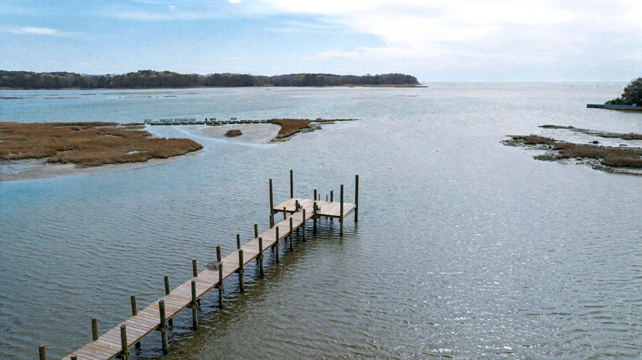 A wooden pier extending into a calm body of water with a distant shoreline.