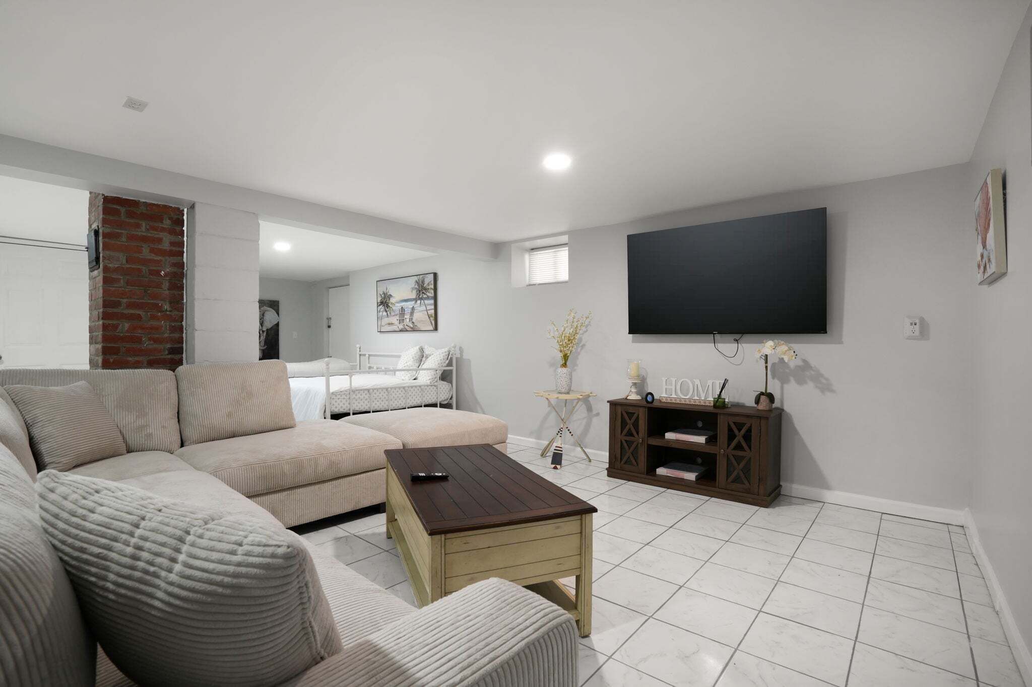 A modern living room with a sectional sofa, a coffee table, a flat-screen TV, and a brick accent wall.