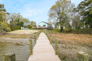 A wooden boardwalk leading to a house with a porch, surrounded by trees and a body of water. - Blissful Oasis | Waterfront Seclusion with a Dock! (Exmore)