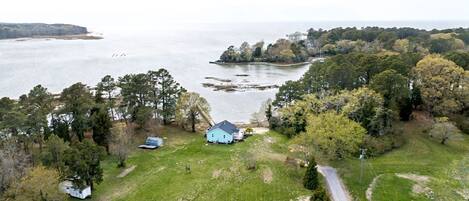 An aerial view of a property with a house, a boat, and a forested area near a body of water.