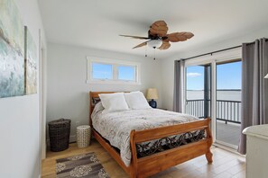 Camera da letto con un letto in legno, una ventola a soffitto, una finestra, un balcone con vista e un cestino.