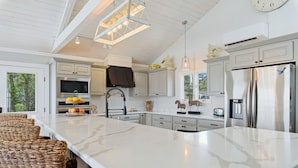 A spacious kitchen with a large island, white cabinetry, and a hanging light fixture. - Salty Oyster | Waterfront living at it (Chincoteague Island)