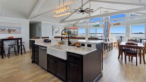 A spacious kitchen with a large island, wooden flooring, and a high ceiling with exposed beams. - Salty Oyster | Waterfront living at it (Chincoteague Island)