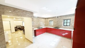 A modern kitchen with red cabinets, a marble countertop, and a view of the dining area. - 2-bedroom villa in charming Thodupuzha with cool AC (THODUPUZHA)
