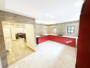 A modern kitchen with red cabinets, a marble countertop, and a view of the dining area. - 2-bedroom villa in charming Thodupuzha with cool AC (THODUPUZHA)