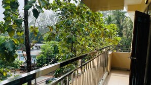 A balcony with a metal railing, a door, and a view of greenery and buildings. - 2-bedroom villa in charming Thodupuzha with cool AC (THODUPUZHA)