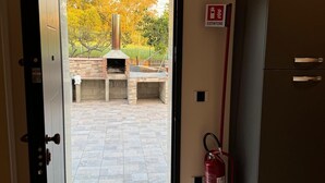 Eine offene Tür, die auf eine Terrasse mit Kamin aus Ziegelsteinen und einem an der Wand befestigten Feuerlöscher führt.