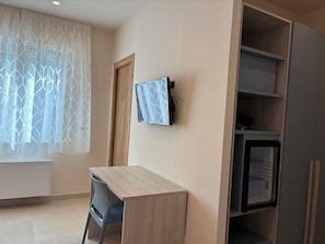 Ein Zimmer mit Schreibtisch, Stuhl, Fernseher und integrierten Regalen.