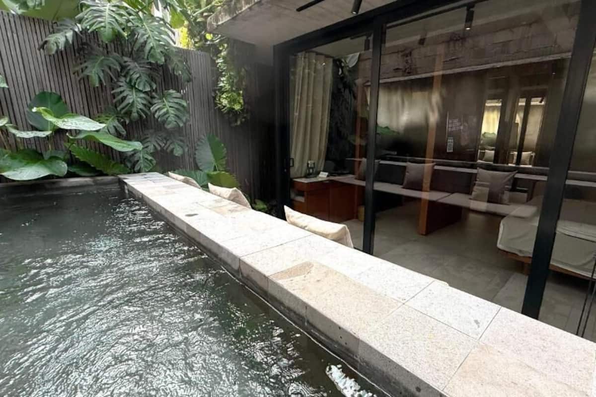Ein moderner Innenpoolbereich mit Steinrand, einer Sitzecke mit Kissen und einer Glaseinteilung.