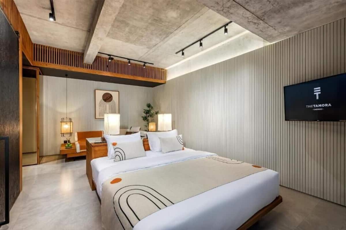 Ein modernes Hotelzimmer mit einem großen Bett, zwei Nachttischen mit Lampen, einem Wand-Fernseher und einer Holzdeckenkonstruktion.