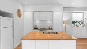 Una cocina moderna con armarios blancos, una isla de madera con un lavamanos y un refrigerador empotrado.