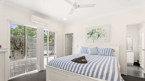A bedroom with a large bed, a ceiling fan, and a view through the glass door. - Coastal 4-Bed Retreat with Pool in Toogoom (Toogoom)