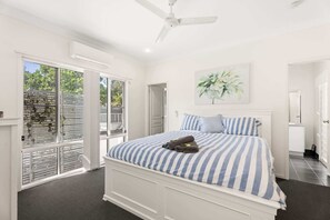 A bedroom with a large bed, a ceiling fan, and a view through the glass door. - Coastal 4-Bed Retreat with Pool in Toogoom (Toogoom)