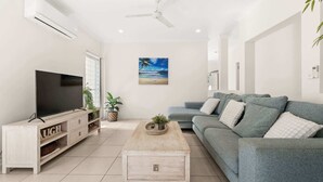 A living room with a flat-screen TV, a grey sofa, a wooden coffee table, and a ceiling fan. - Coastal 4-Bed Retreat with Pool in Toogoom (Toogoom)