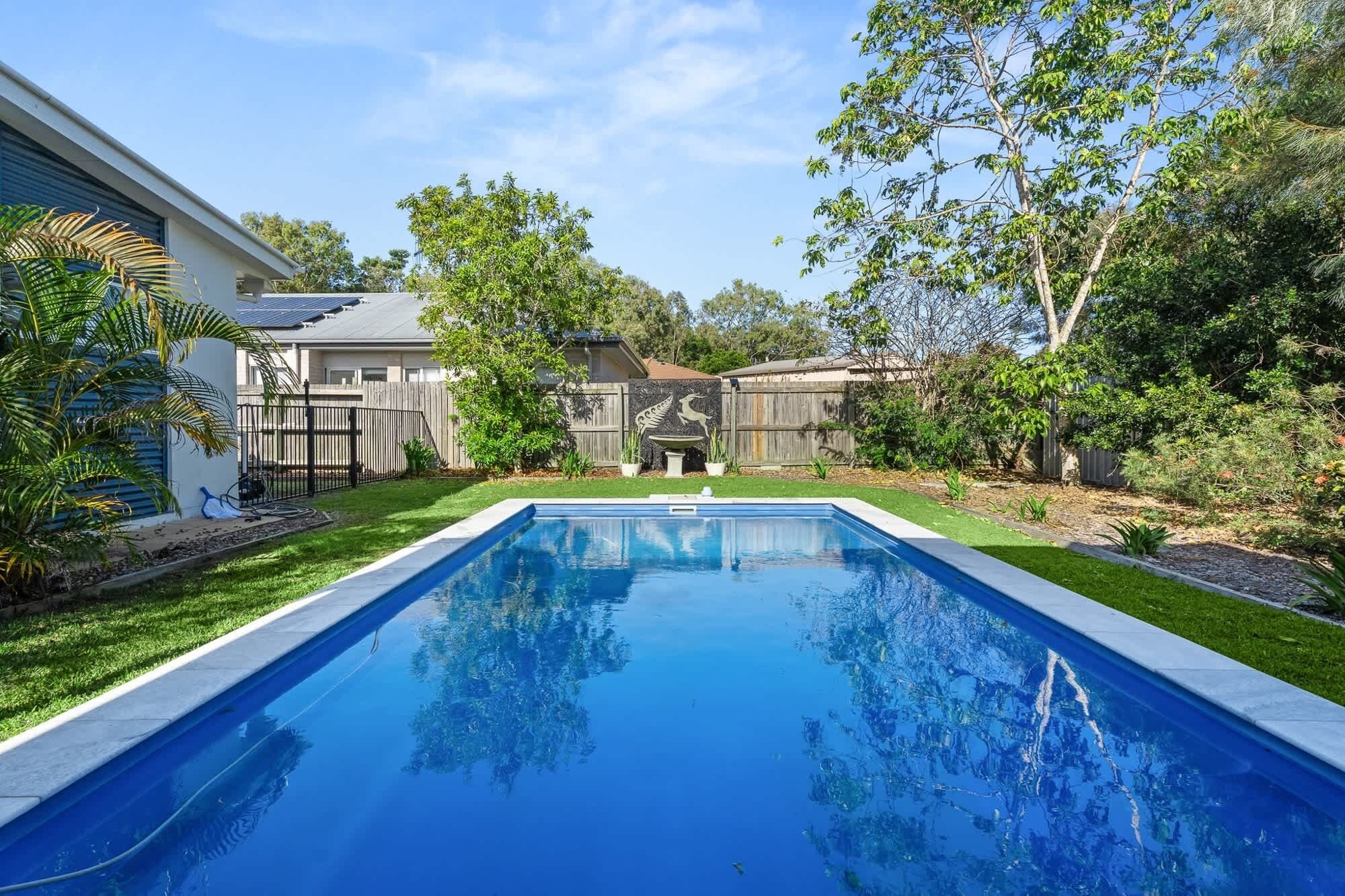 A rectangular swimming pool with a clear blue water surface, surrounded by a well-maintained lawn and various trees.