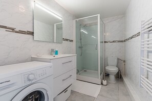 Ett modernt badrum med tvättmaskin, en dusch med glasväggar, en toalett och en stor spegel.