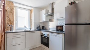 Et moderne køkken med hvide skabe, et rustfrit stål køleskab, en opvaskemaskine og et vindue med udsigt.