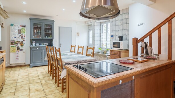 Una cocina con una isla central, sillas de madera, estufa integrada y un mueble con puertas de vidrio.