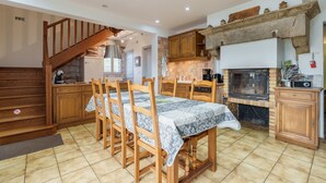 Una cocina con armarios de madera, una mesa de comedor con sillas, un horno empotrado y una escalera.