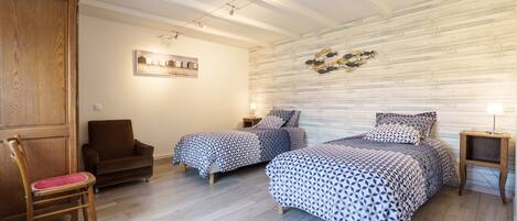 A bedroom with two beds, a wooden wardrobe, a chair, and a wall-mounted light fixture.