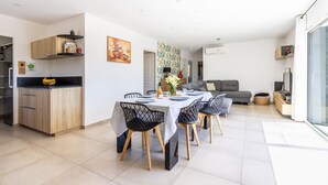 Una cucina moderna con mobili in legno, un'area pranzo con tavolo e sedie, un divano grigio e una televisione.