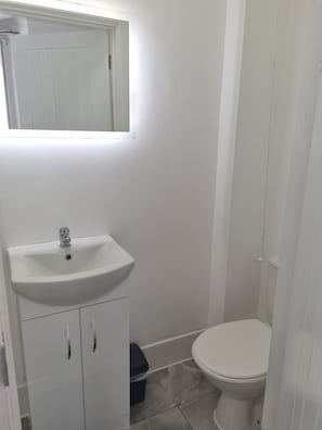 Ein kleines, weißes Badezimmer mit Waschbecken, Toilette und Spiegel über dem Waschbecken.
