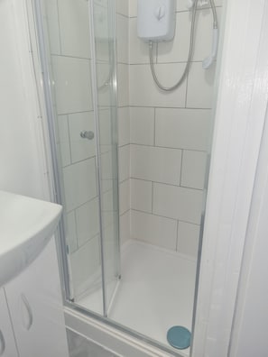 Eine Dusche mit Glastür, eine weiße Fliesenwand und eine blaue Badmatte.