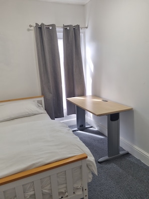 Ein Schlafzimmer mit Bett, kleinem Schreibtisch und einem fenster mit Vorhängen.