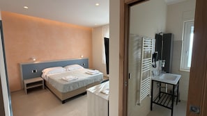 A modern hotel room with a large bed, bedside tables, a built-in heater, a small bathroom with a sink and mirror, and a view of the outside. - B&B Capo Vaticano Stay (Ricadi)