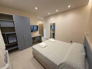 A bedroom with a bed, a desk, a TV, and a wardrobe.