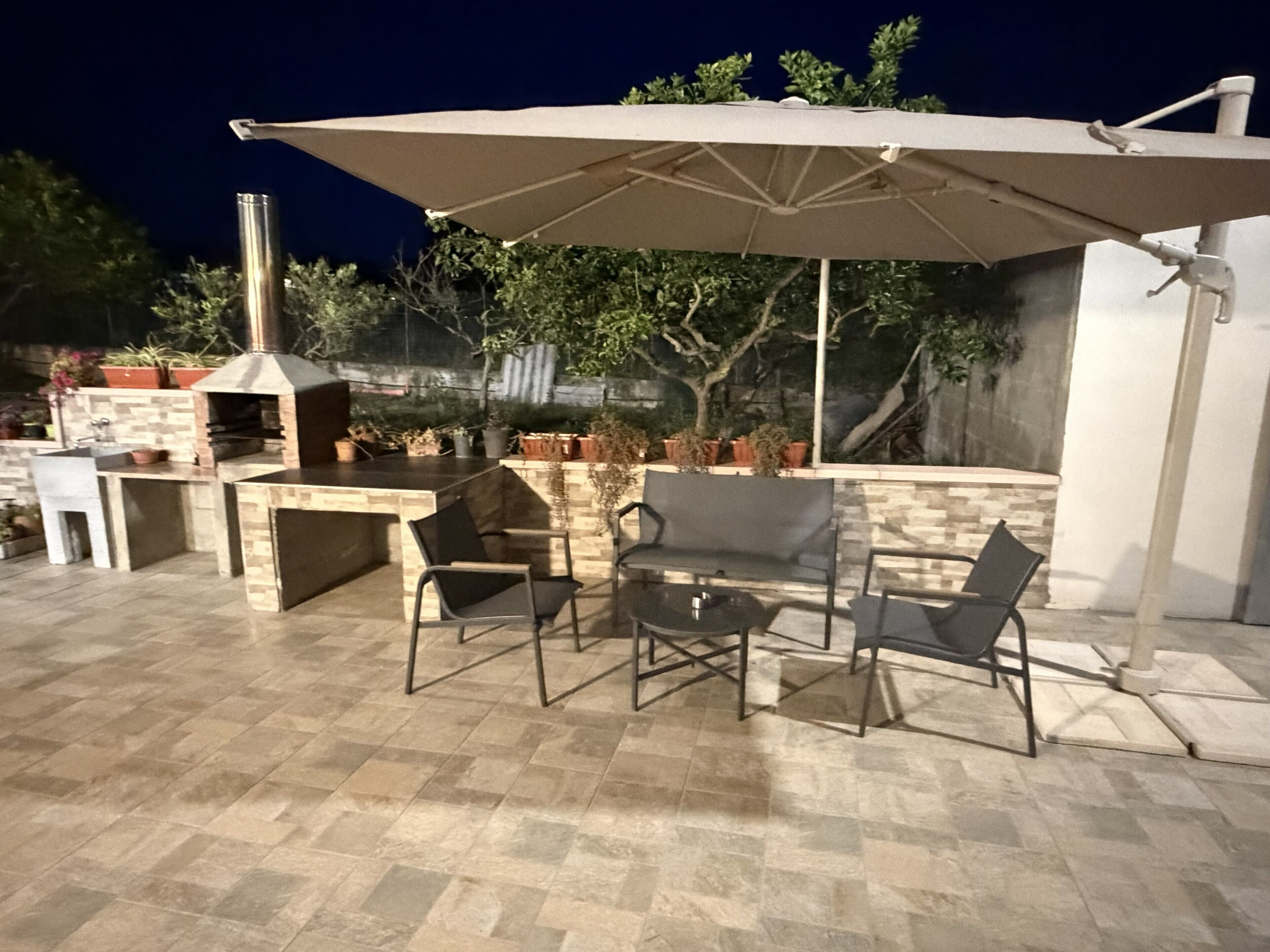 An outdoor patio with a grill, chairs, and an umbrella.