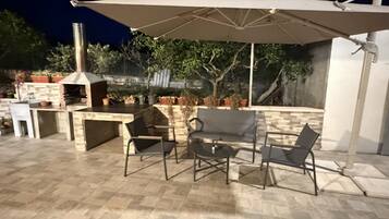 An outdoor patio with a grill, chairs, and an umbrella.