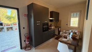 A compact kitchen with dark cabinetry, a built-in oven, and a dining area with a table set for two. - B&B Capo Vaticano Stay (Ricadi)
