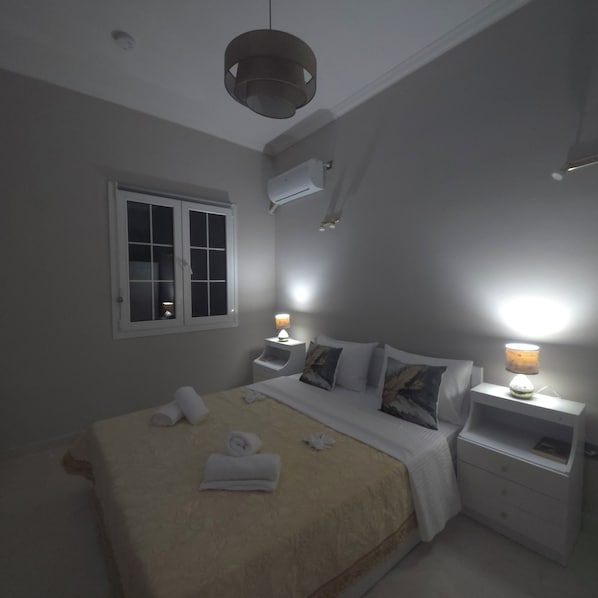A bedroom with a bed, two bedside tables, a window, and an air conditioning unit.
