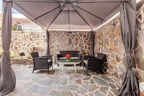 Un patio al aire libre con muros de piedra, un espacio de descanso cubierto y una mesa con sillas.