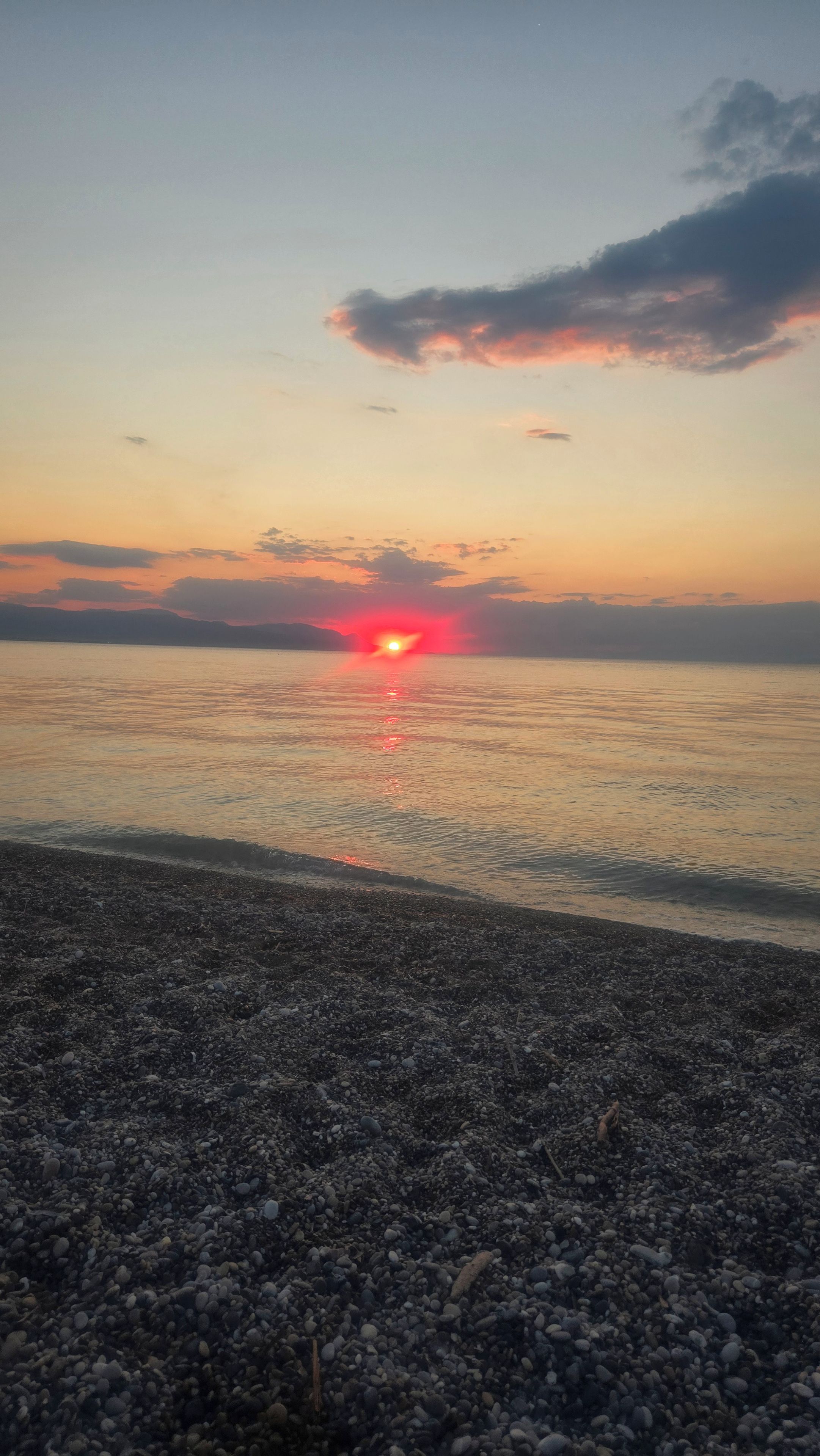 Uma praia com pedras e um pôr do sol sobre a água.