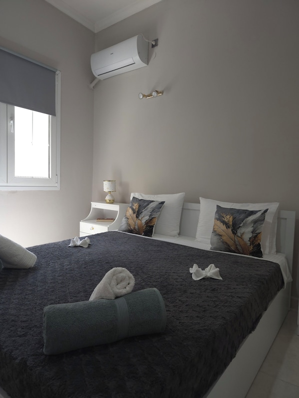 A hotel room with a bed, pillows, a nightstand, a lamp, and an air conditioning unit.
