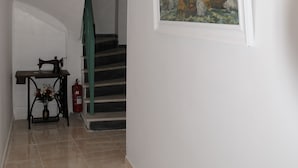 En hall med en kristallkrona, en målning av skepp, en symaskin och en trappa.