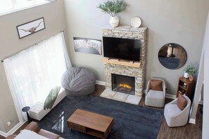 A living room with a stone fireplace, a flat-screen TV, a sofa, a bean bag, and a coffee table. - Peach State Hideaway, The Columbus Escape (Columbus)